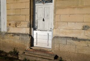 Porte ancienne en bois équipée d'une barrière anti inondation à la base, protégeant la façade en pierre usée des risques d'inondation.