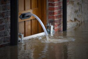 Barrière anti inondation installée sur une porte en bois, avec un tuyau de drainage évacuant l'eau de l'intérieur pendant une inondation.